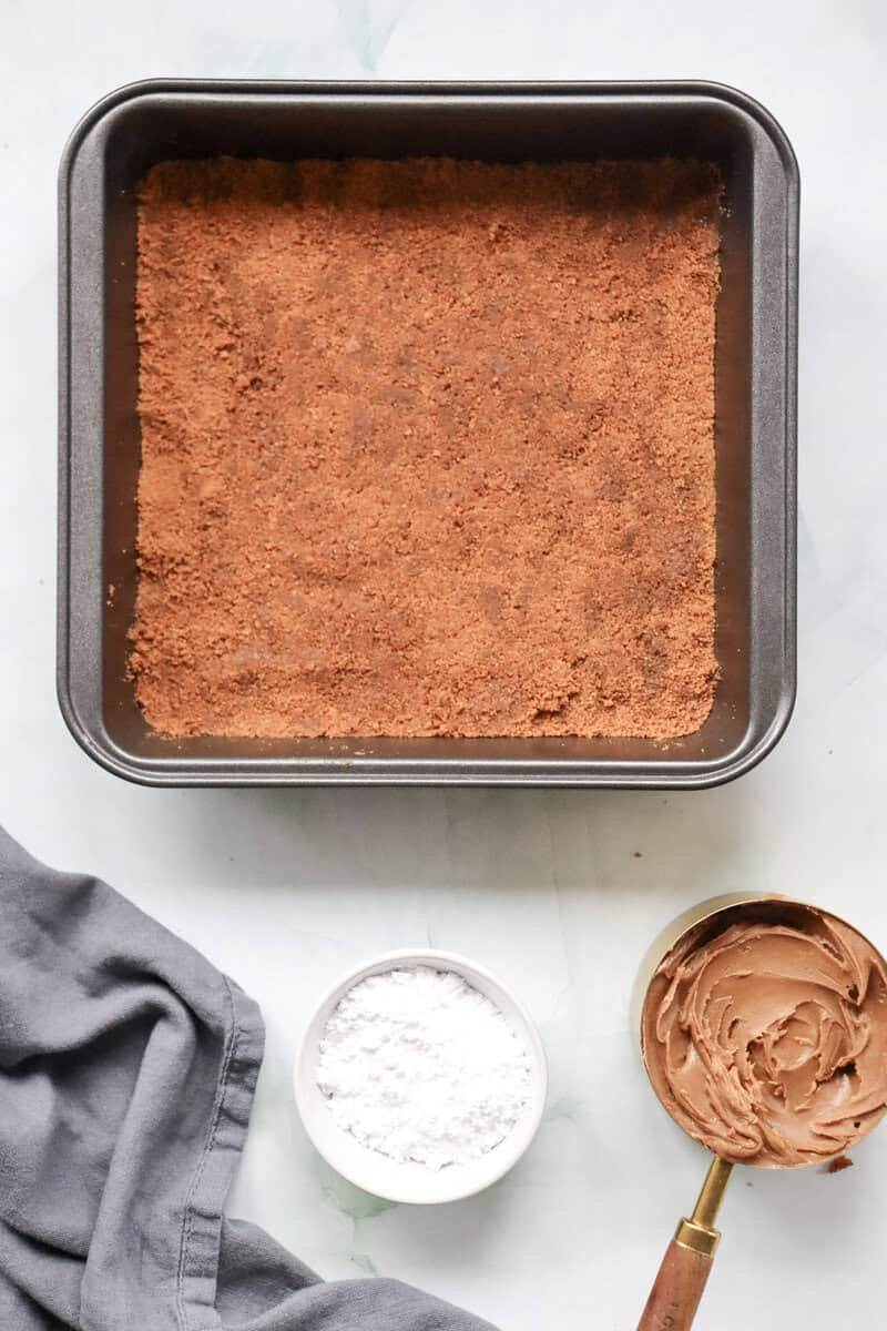 Cruhed Biscoff cookies pushed down in a square pan to form a crust.