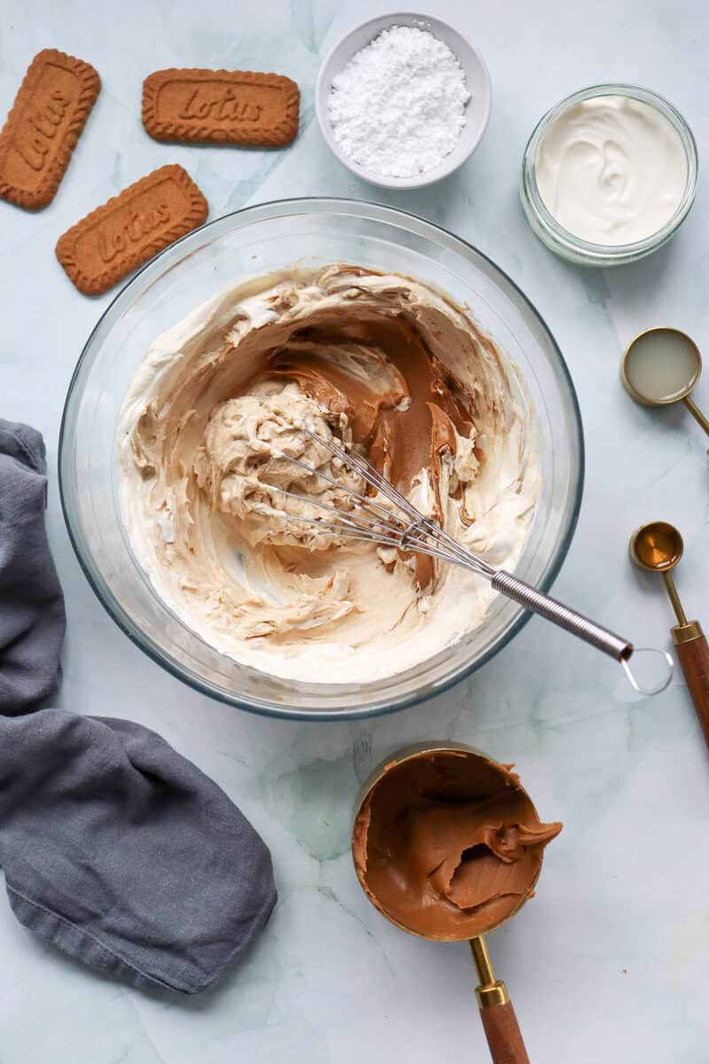 Cream cheese, powdered sugar, vanilla extract, and cookie butter in a glass mixing bowl with a whisk.