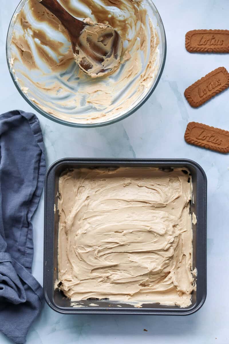 An empty mixing bowl near a square pan holding a Biscoff cheesecake.