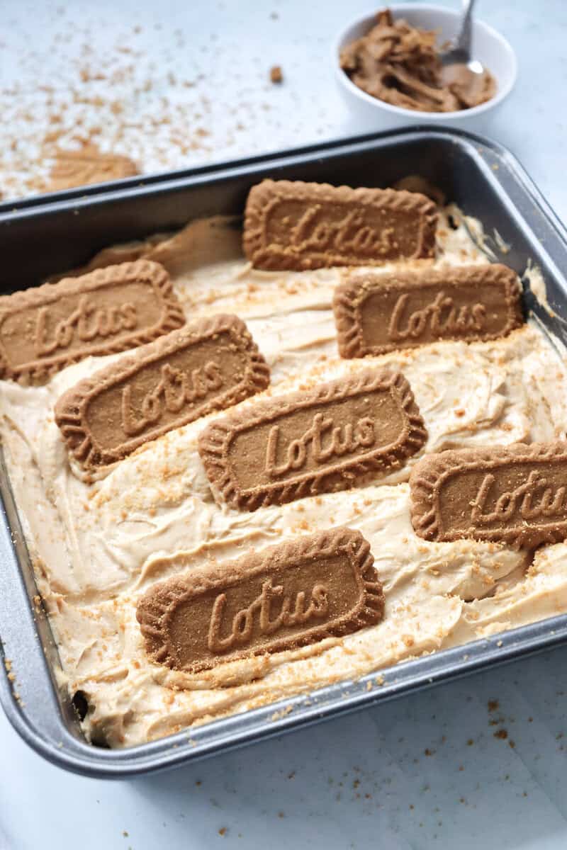 A no bake cheesecake topped with Biscoff cookies in a square metal pan.