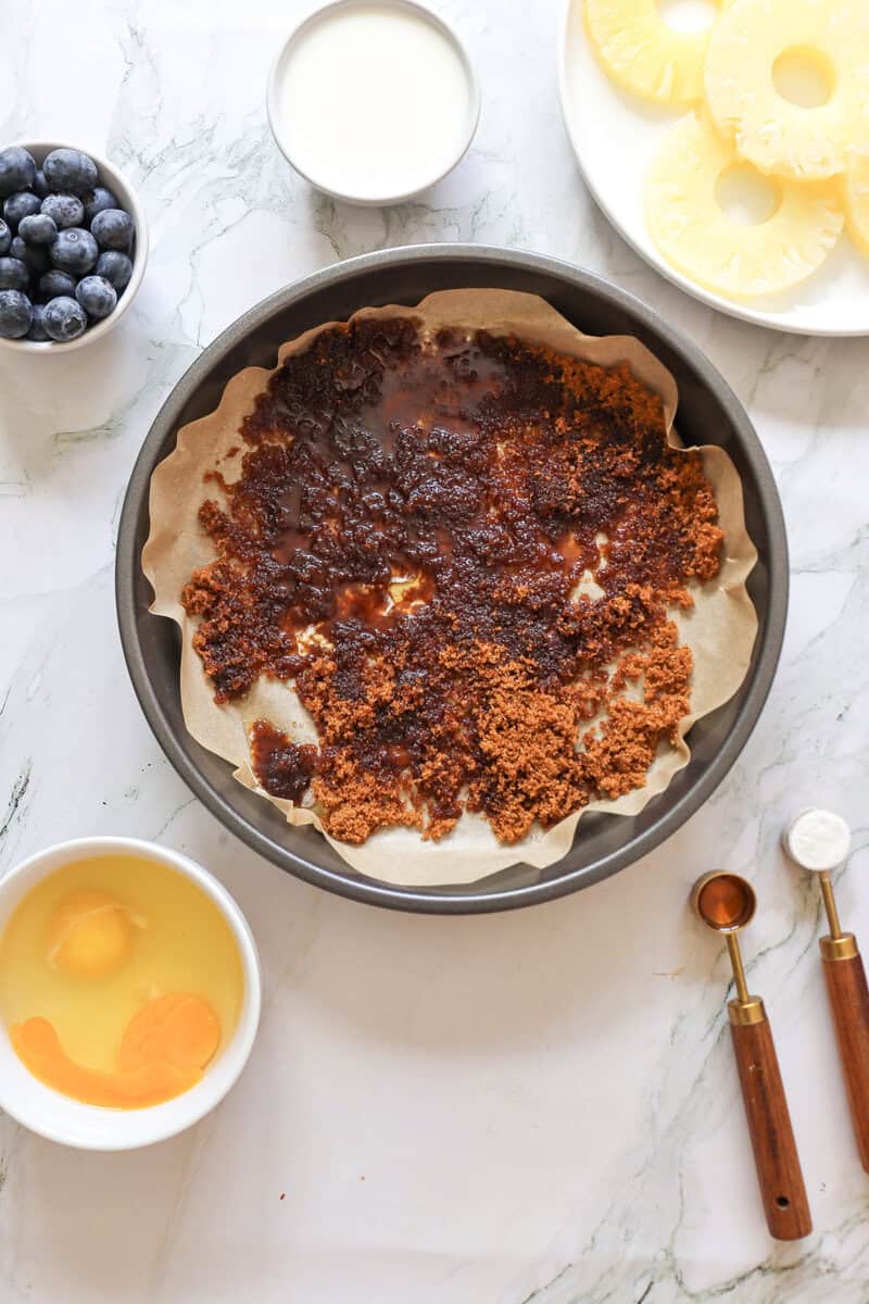 A pie pan filled with parchment paper, melted butter, and brown sugar.