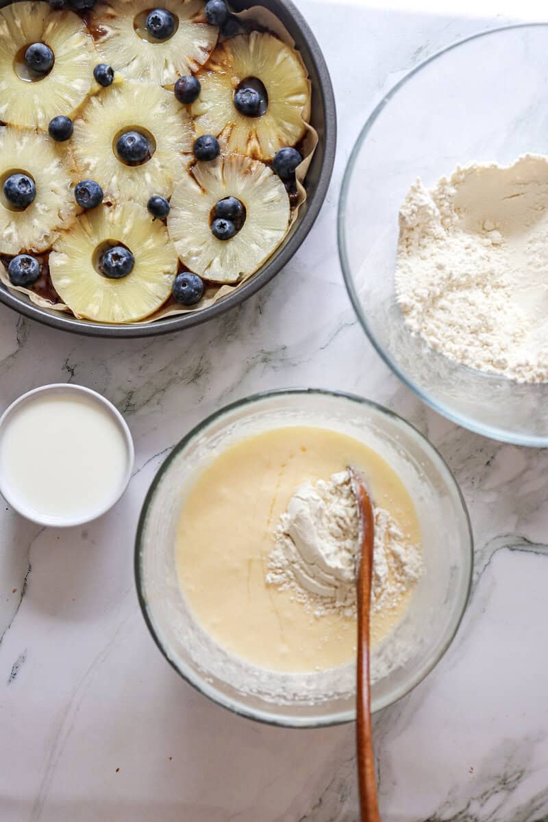 Dry ingredients being added to wet ingredients in a glass mixing bowl to make a cake batter.