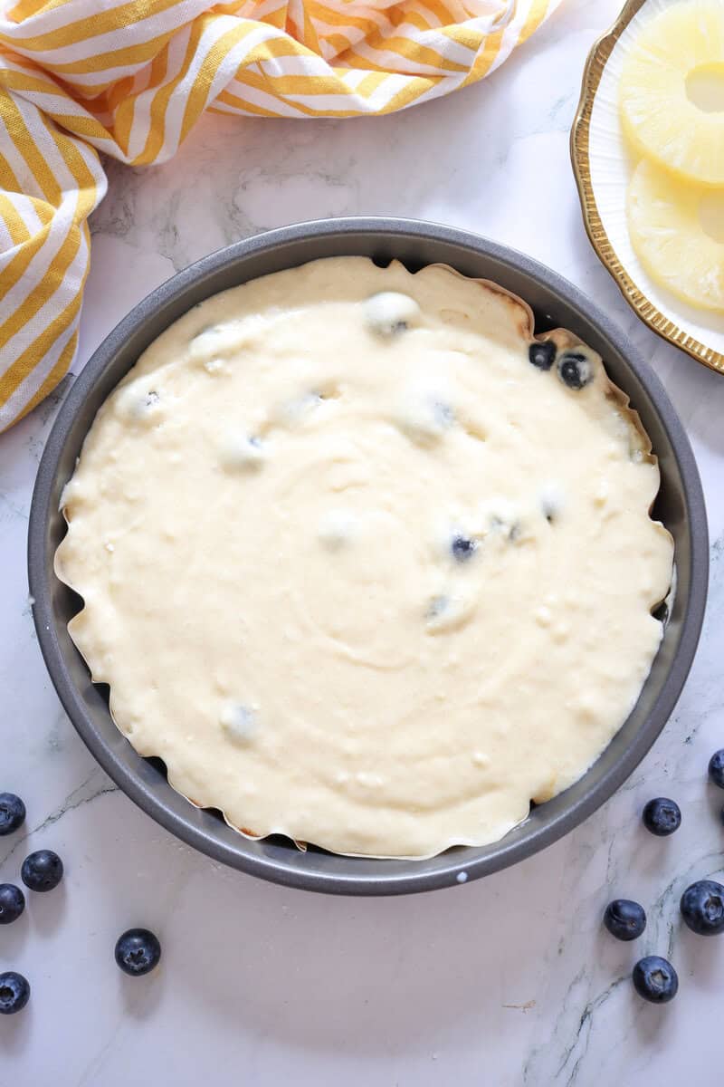 Cake batter in a metal cake pan with blueberries poking through.