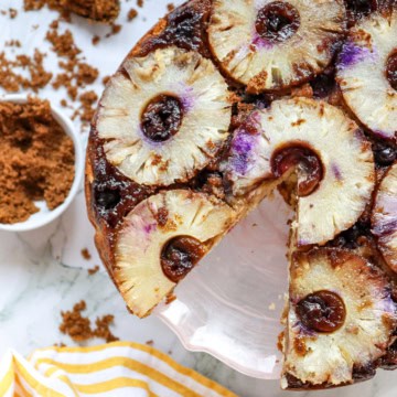A blueberry pineapple cake on a white cake stand with a slice missing.