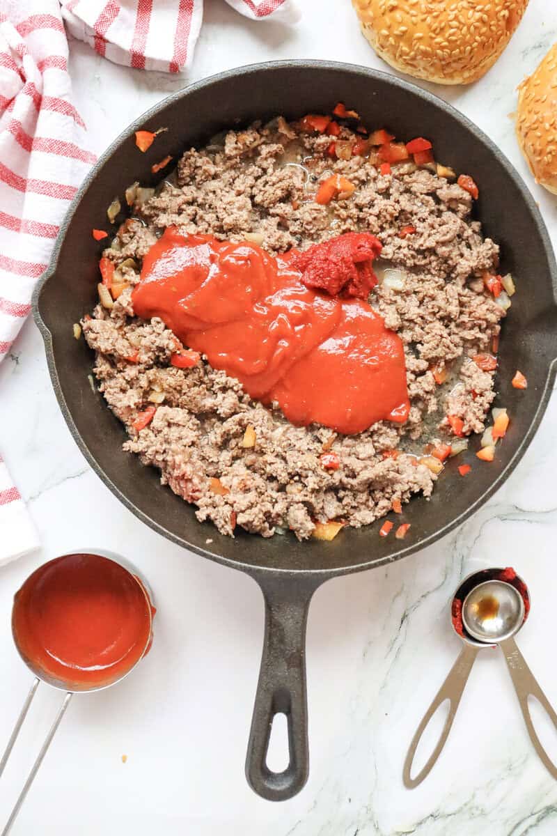 A cast iron skillet full of ground beef and vegetables with a tomato sauce and tomato paste on top.