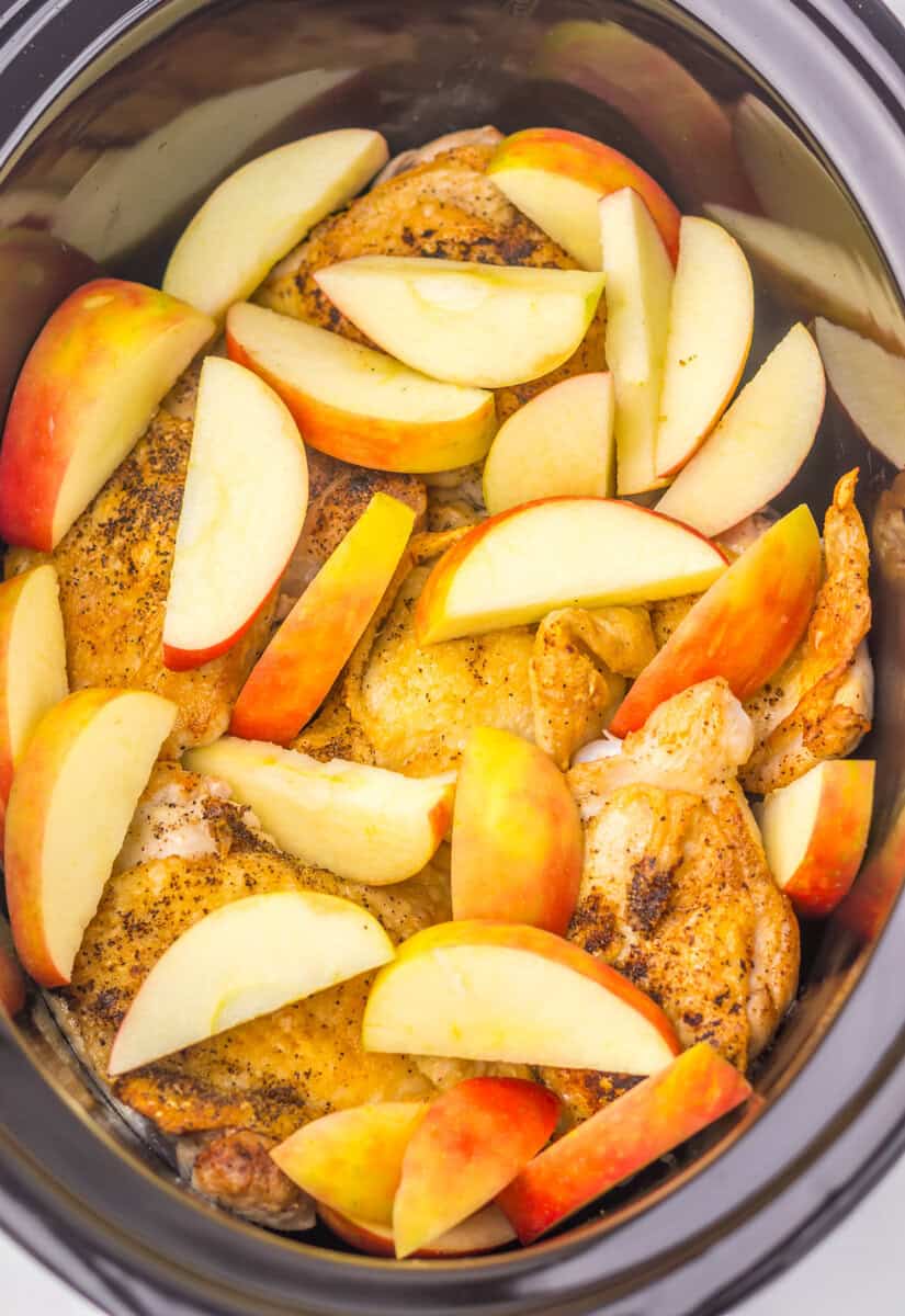 Chicken thighs and apple slices in a slow cooker.