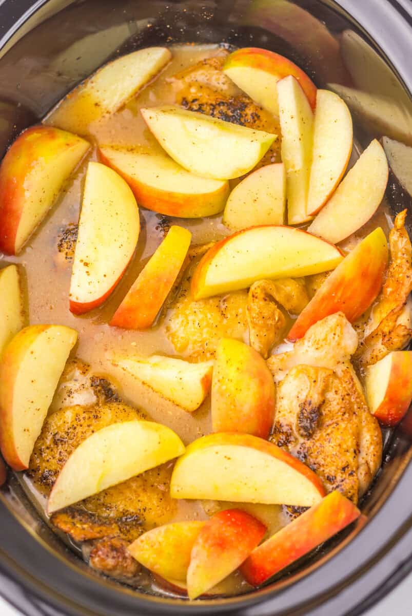 Chicken thighs and apple slices in a slow cooker with apple cider sauce.