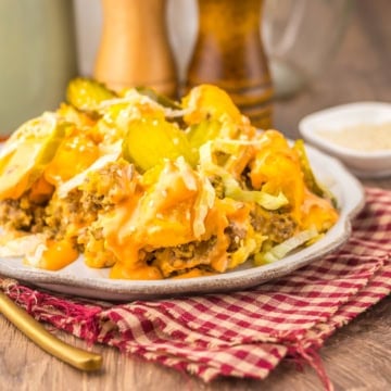 A plate of casserole topped with melted cheese, pickles, and shredded lettuce sits on a red checkered cloth with a fork, salt, and pepper shakers nearby.
