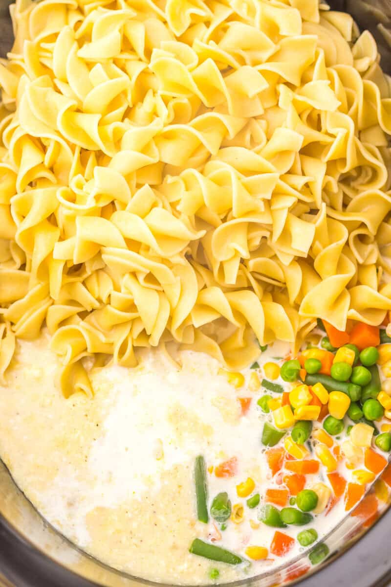 Adding the egg noodles to the slow cooker with the rest of the ingredients.