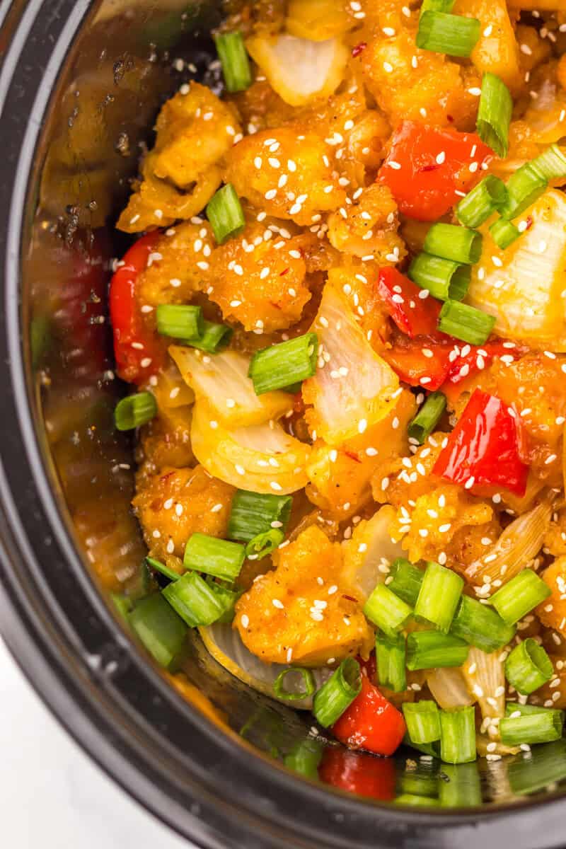 Chinese food topped with green onions and sesame seeds in a black crock pot.