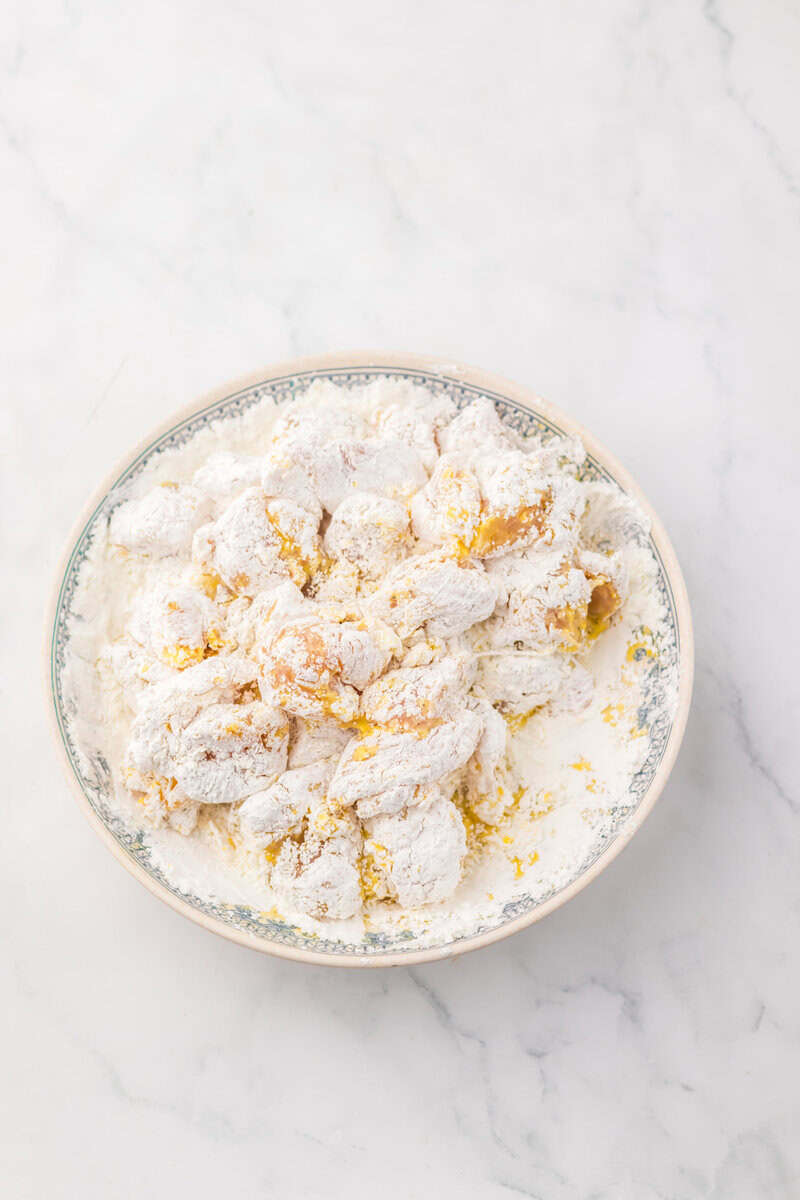 Cooked chicken in a blue and white bowl on a white marble countertop.