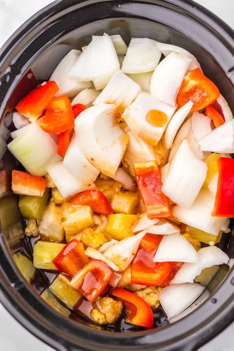 A slow cooker of vegetables, pineapple, chicken, and a brown sauce.