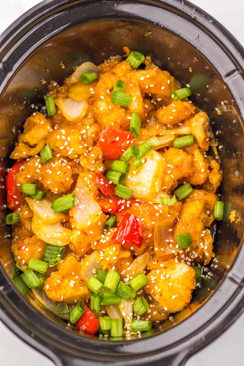 Chinese-style chicken dish in a black slow cooker topped with green onions and sesame seeds.