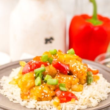 SweetFire Chicken on white rice on a grey plate. A red bell pepper can be seen in the background.