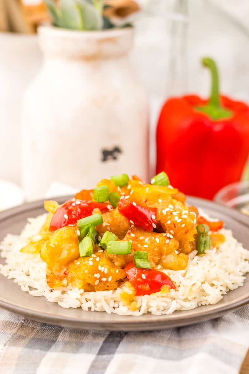 SweetFire Chicken on white rice on a grey plate. A red bell pepper can be seen in the background.