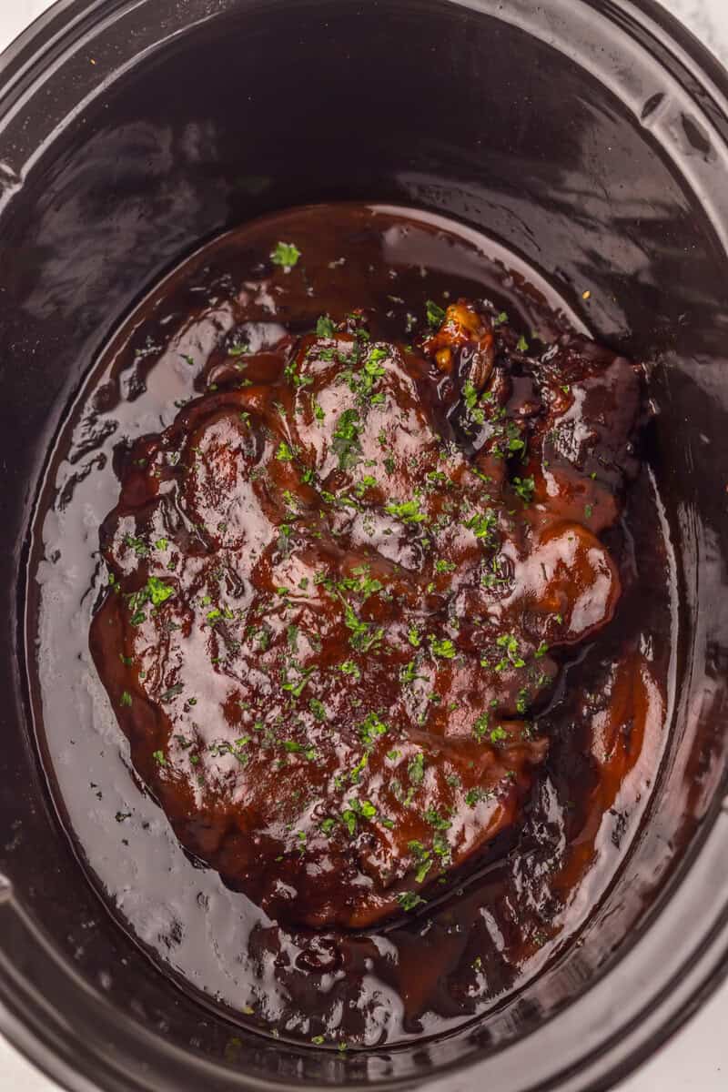 Dr. Pepper BBQ beef in a slow cooker topped with chopped parsley.