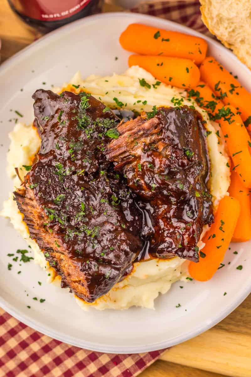 A plate of Dr. pepper beef roast over mashed potatoes with cooked carrots in the side.