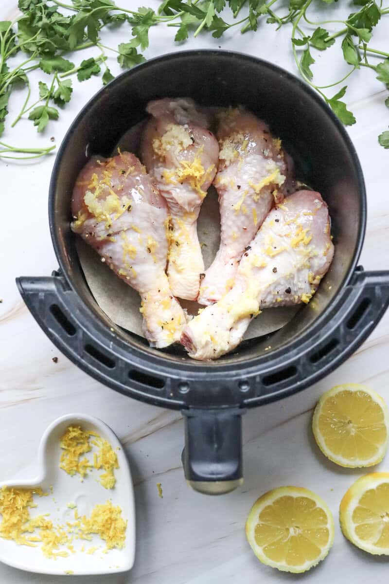 An air fryer basket with 4 chicken drumsticks covered in lemon garlic seasoning.