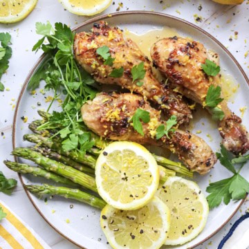 Air fryer drumsticks on a white plate with asparagus and lemon slices, topped with parsley.