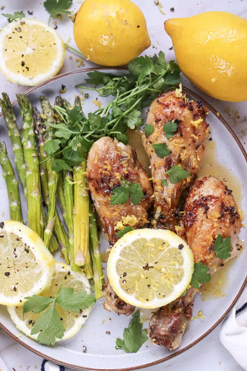 A plate of air fryer lemon chicken, asparagus, and lemon slices.