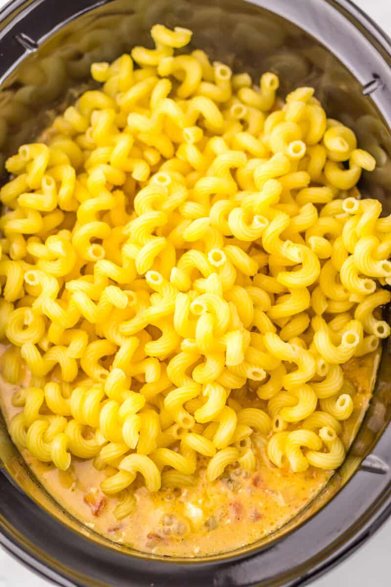 Cooked pasta on top of a Rotel dip sauce in a slow cooker.
