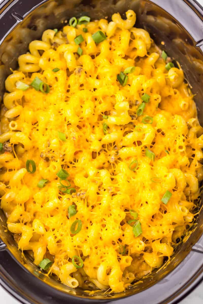 Pasta with cheese and Green onions in a black slow cooker.