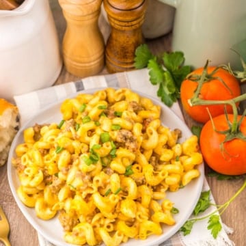 Rotel Pasta in a white bowl on a cloth napkin with wooden grinders and tomatoes in the background.