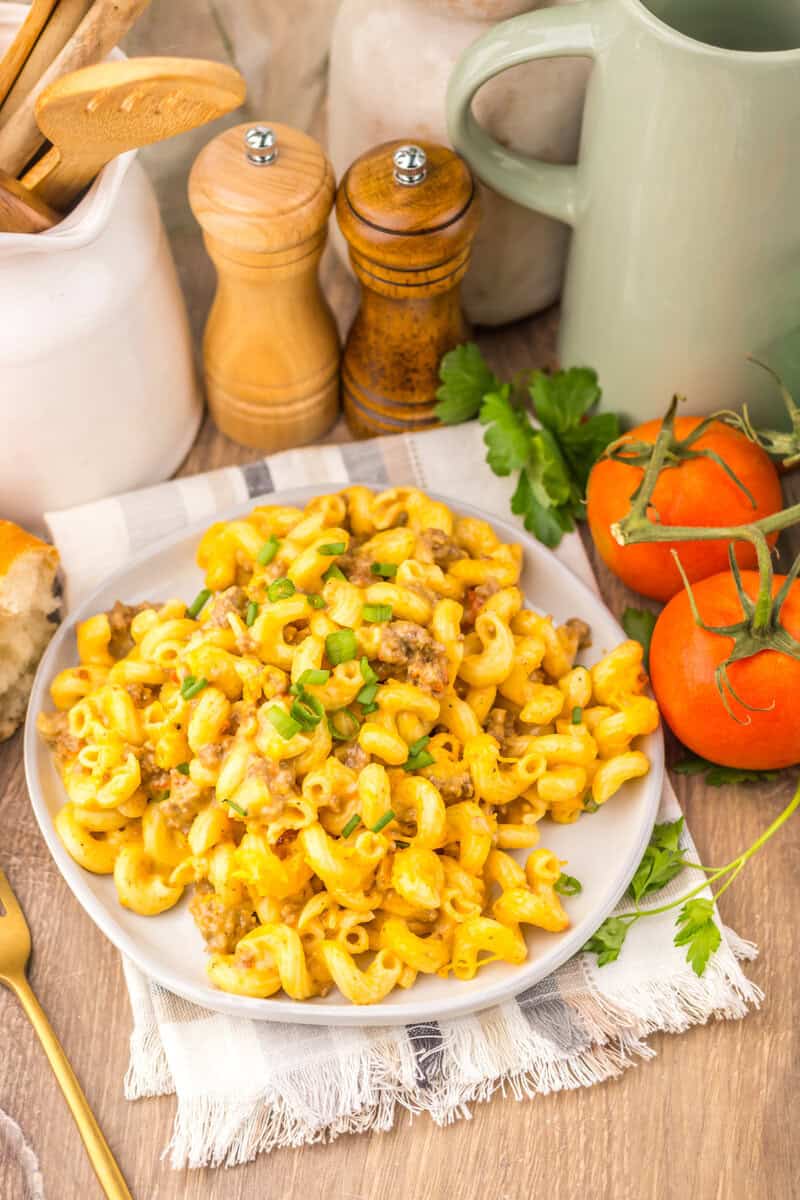 Rotel Pasta in a white bowl on a cloth napkin with wooden grinders and tomatoes in the background.