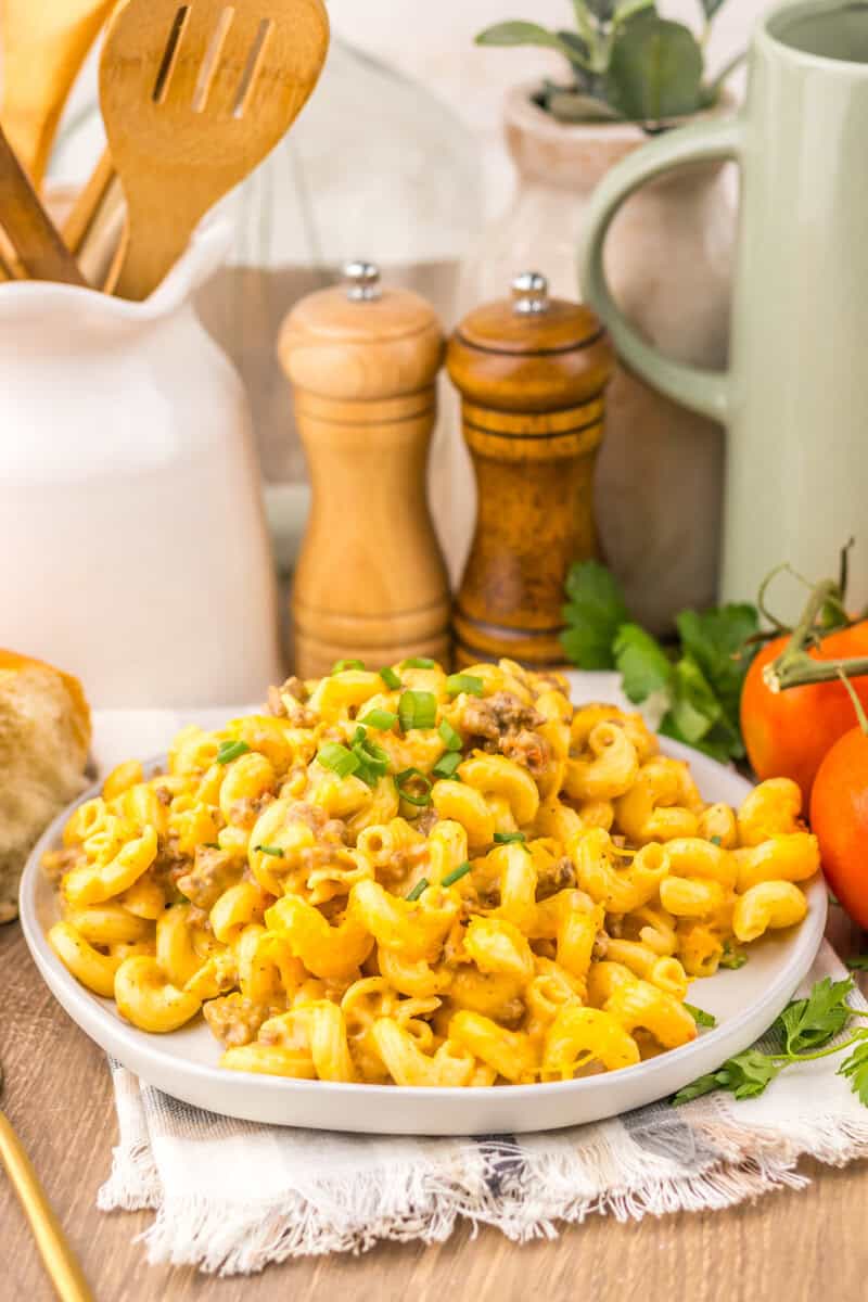 A white plate of Rotel pasta with herbs, tomatoes, and wooden pepper and salt grinders in the background.