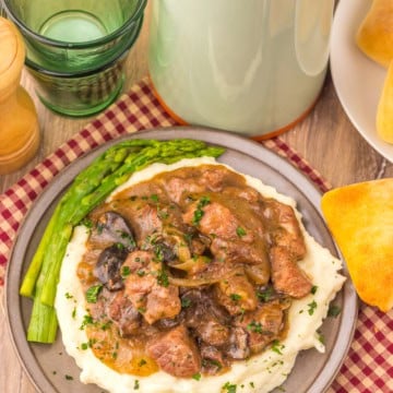 Texas Roadhouse Beef Tips over mashed potatoes on a grey plate.