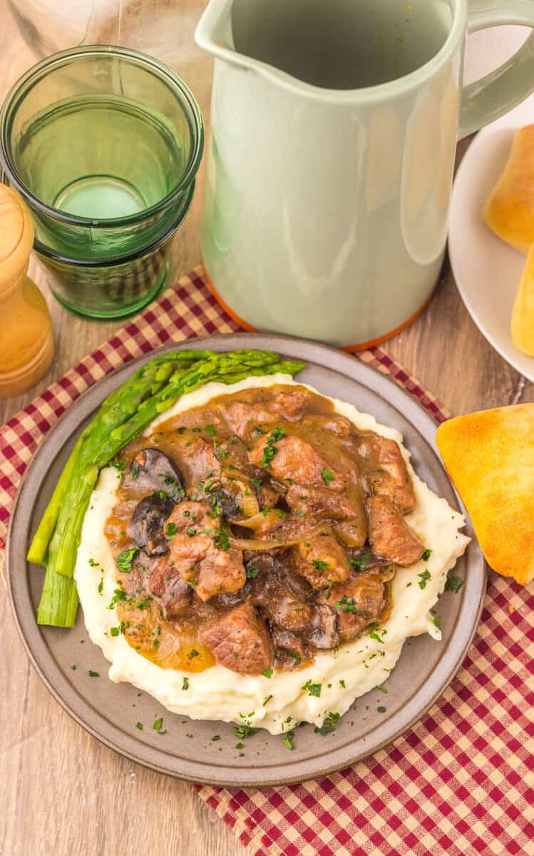 Texas Roadhouse Beef Tips over mashed potatoes on a grey plate.