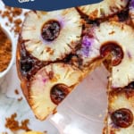 A pineapple blueberry upside down cake sits beautifully on a white plate, accompanied by a striped yellow napkin and bowls of brown sugar and blueberries nearby.