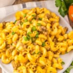 A plate of cheesy slow cooker Rotel pasta with ground meat, topped with chopped green onions, on a white plate with a fork.
