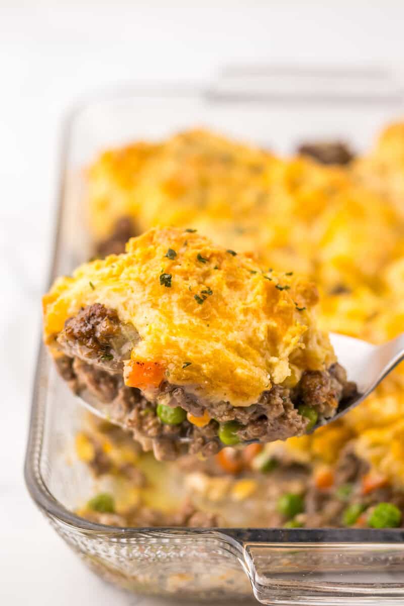 A scoop of Cheddar Bay hamburger casserole on a spoon with the whole casserole seen in the background.