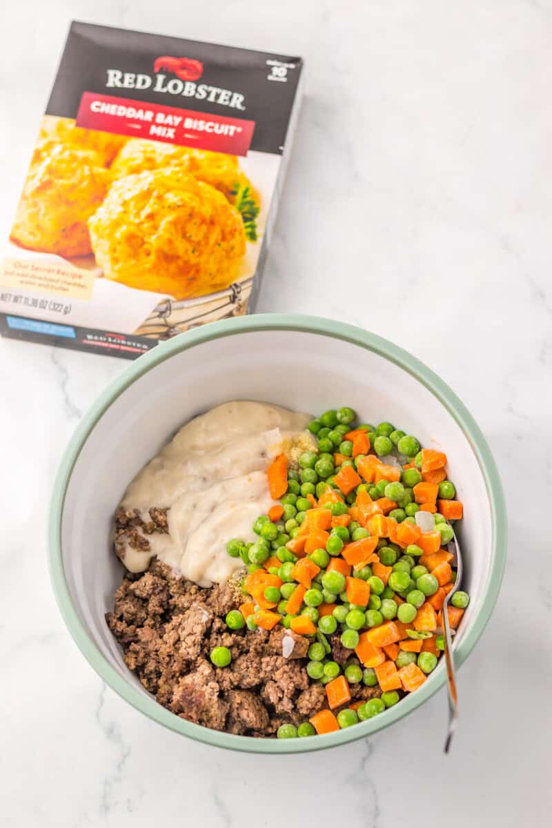 A bowl of ground beef, peas, carrots, and cream of mushroom soup with a spoon.