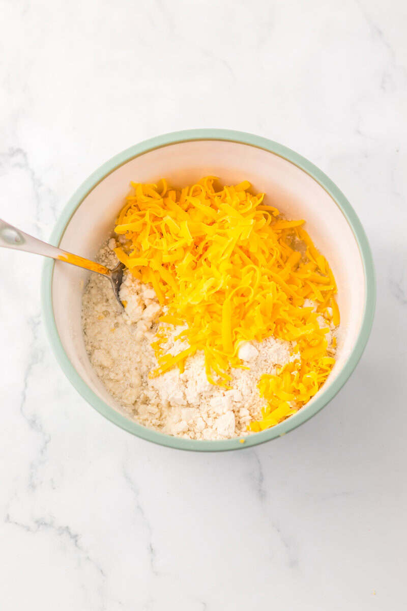 Biscuit mix and shredded cheddar cheese in a light green bowl with a spoon.