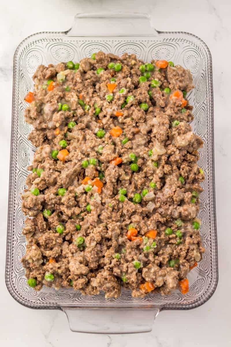 Ground beef and vegetable mixture in a clear glass baking dish on a white surface.
