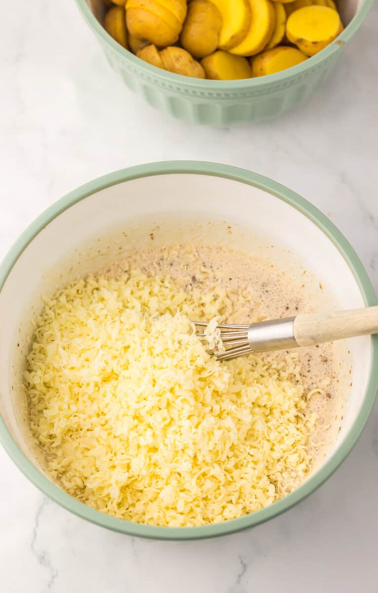 A bowl of creamy French onion sauce with shredded cheese and a whisk.