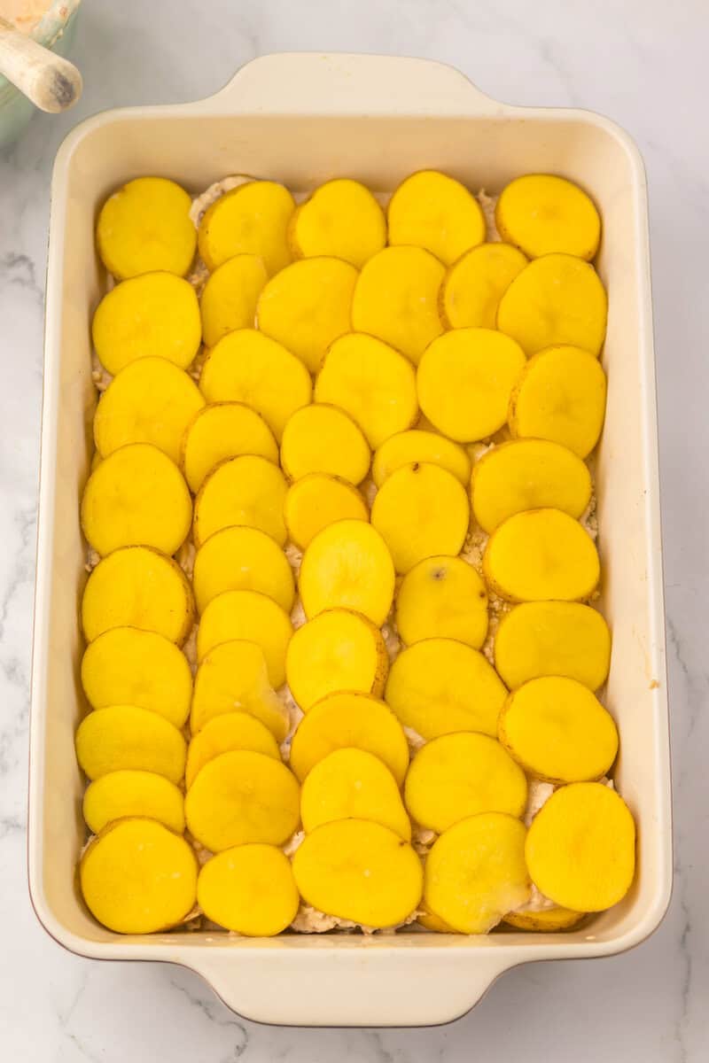 Layers of sauce and potatoes in a white ceramic baking dish.
