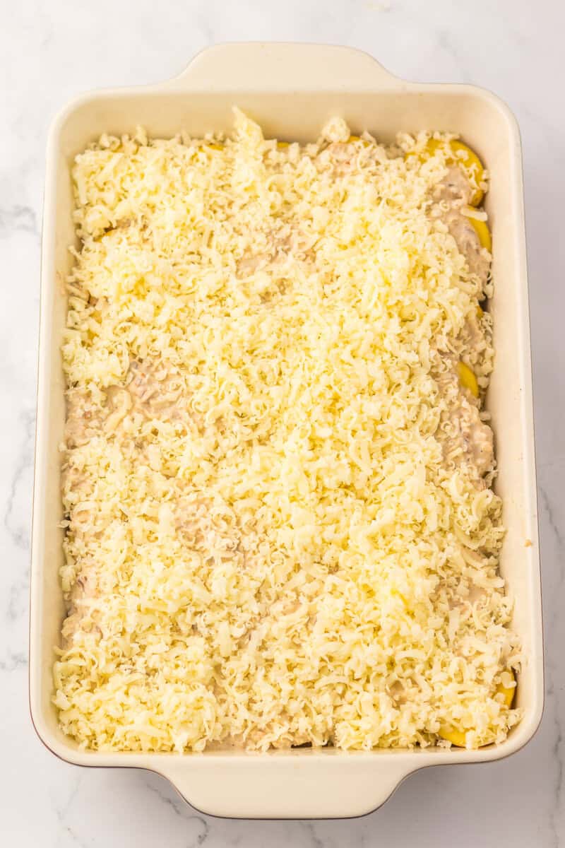 The unbaked casserole topped with shredded cheese on a white marble countertop.