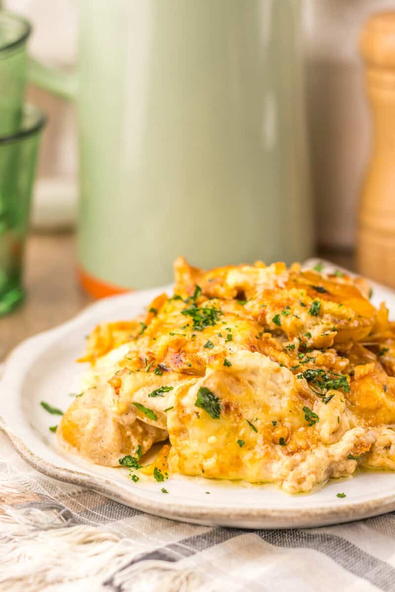 A serving of potato bake with French onion soup on a white plate with a pitcher in the background.