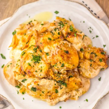 Cheesy potato casserole on a white plate on a wooden surface.