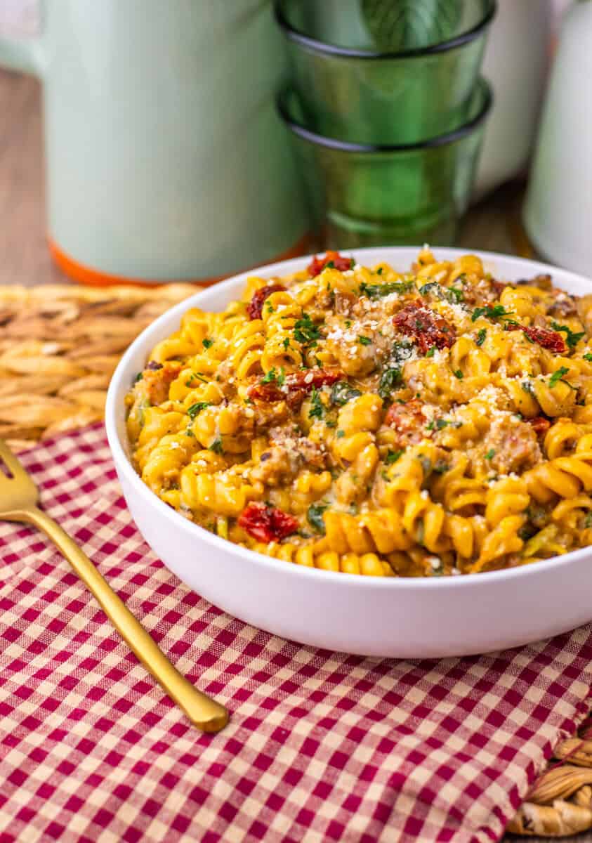 A white bowl of creamy Tuscan pasta on a table with a red and white checkered napkin.