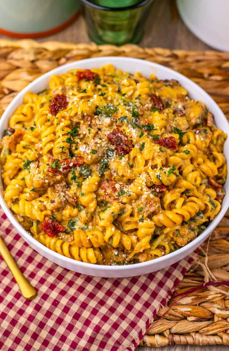 A bowl of Tuscan pasta on a red and white table cloth with a gold fork nearby.
