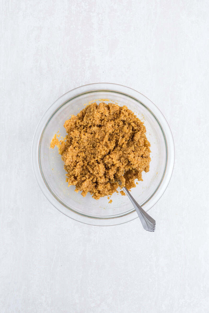 Graham cracker crumbs and butter in a small glass bowl with a fork.