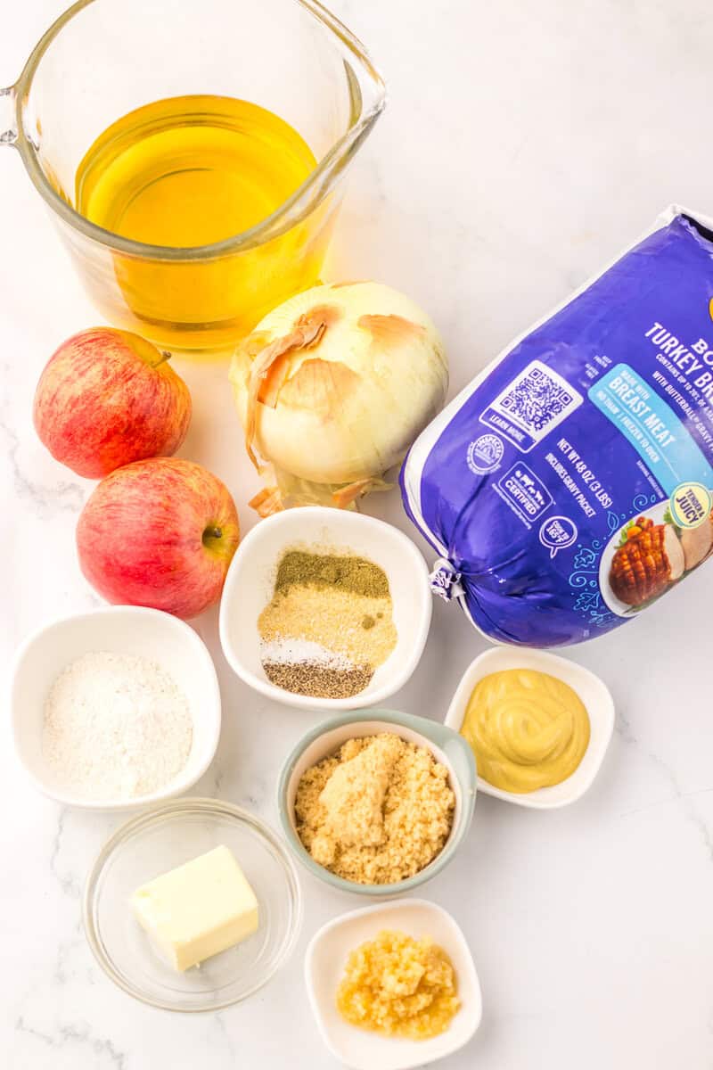 A turkey breast still in the package alongside apples, spices, garlic, brown sugar, and other ingredients in individual bowls.