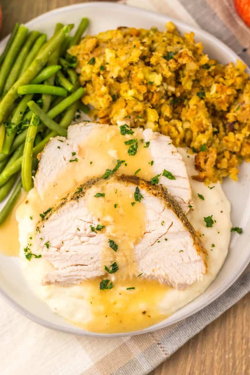A white plate with slow cooker turkey and gravy, green beans, and stuffing.