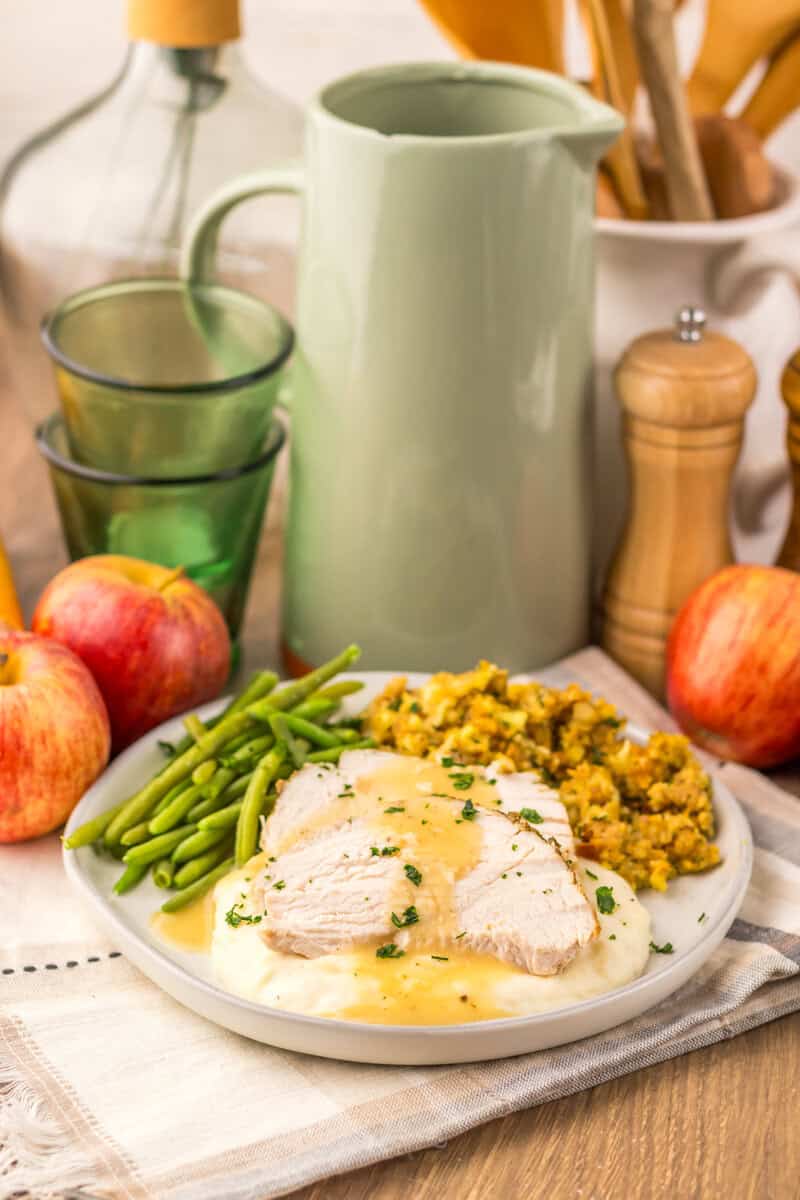 A Thanksgiving plate on a table surrounded by apples, green glasses, a pitcher, and salt shaker.