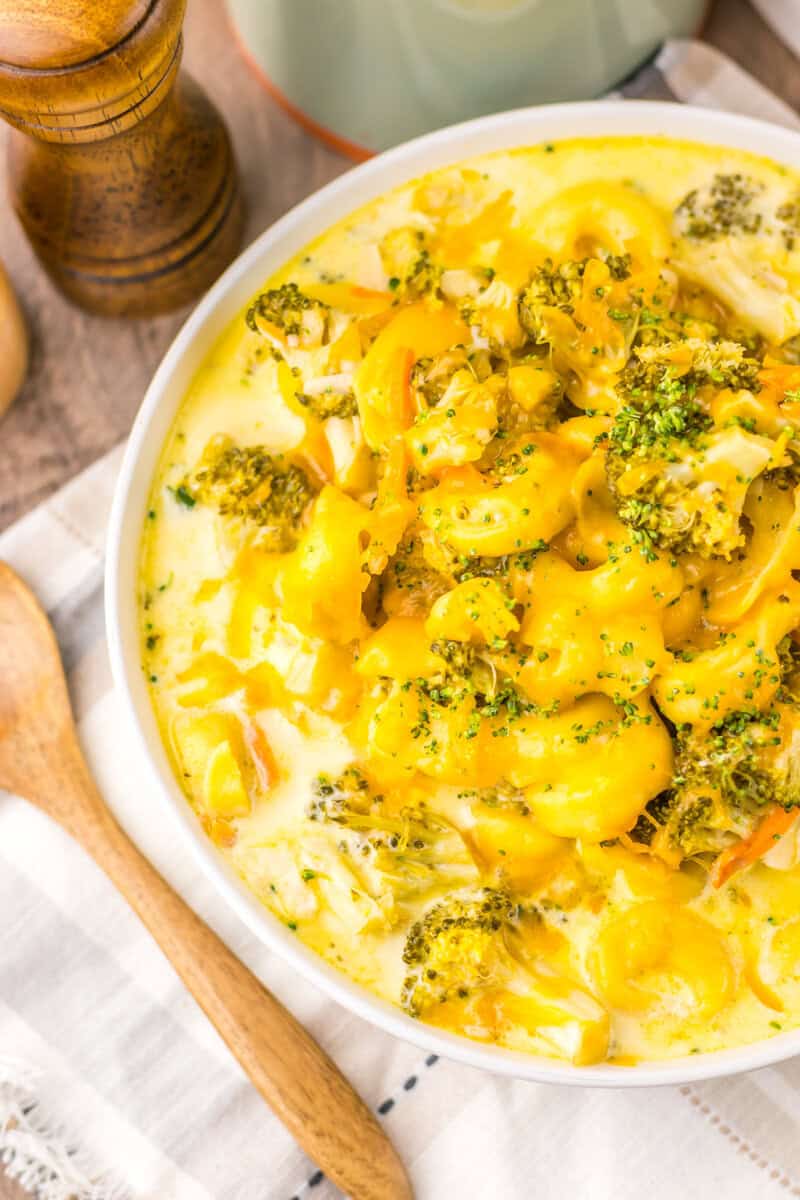 A white bowl of cheese and broccoli tortellini soup with a spoon nearby.