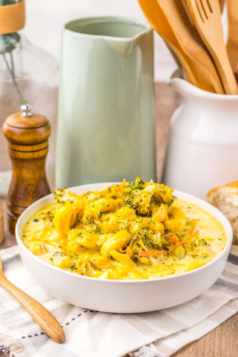 A white bowl of broccoli and tortellini soup with salt and pepper grinders and pitchers in the background.